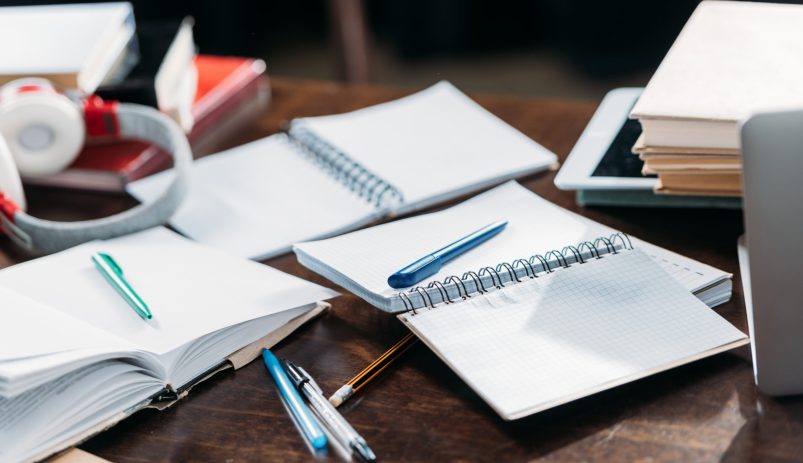 Close-up view of open blank notebooks with pens and books on wooden table