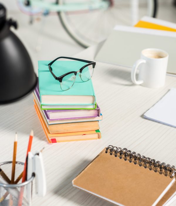 close up view of piles of books, notebooks, folders, cup of coffee and eyeglasses at workplace at