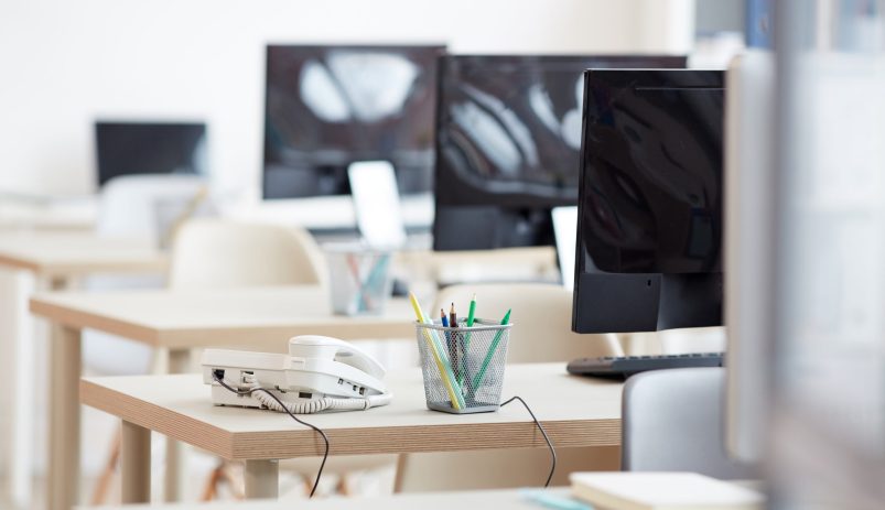 Background image of empty office workplaces in row with focus on wired telephone on desk in call center, copy space