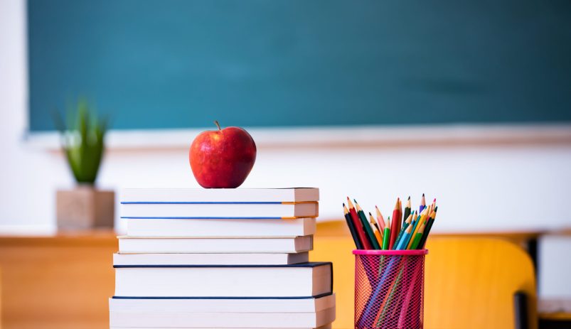 Back to School Concept. Apple, accessories and books in the classroom against chalkboard.