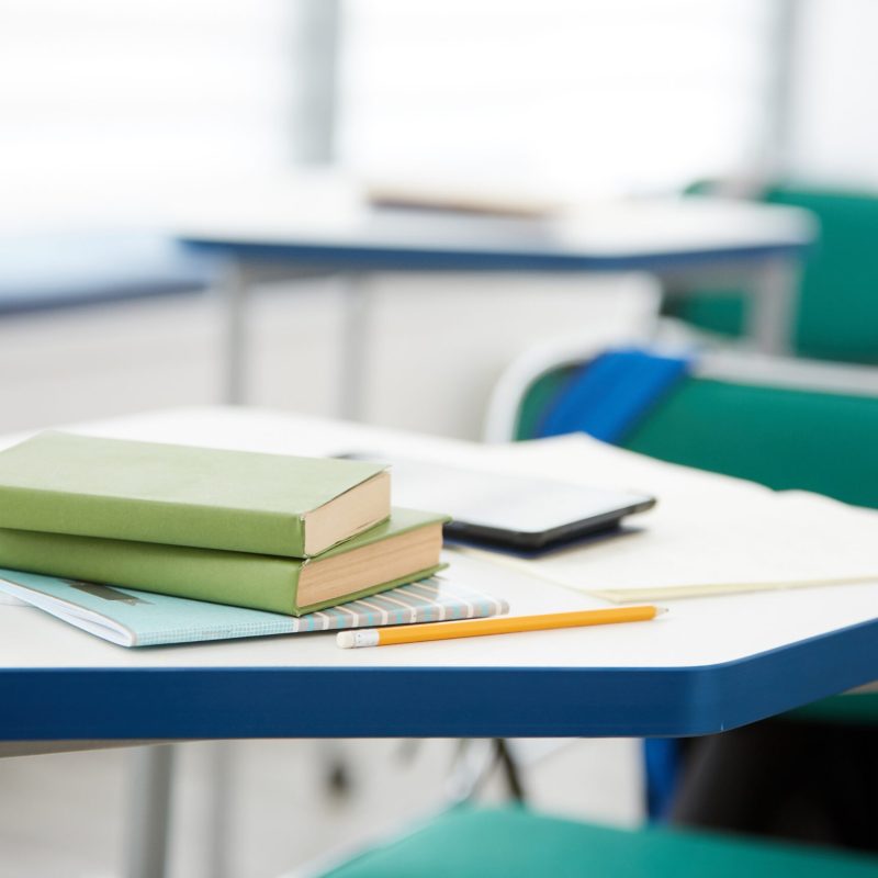 Background close up of green books stacked on desk in school classroom interior, copy space