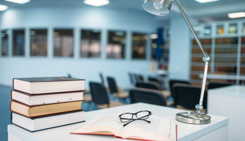 Stack of books and glasses on the table in university library, nobody. Knowledge depository, education concept